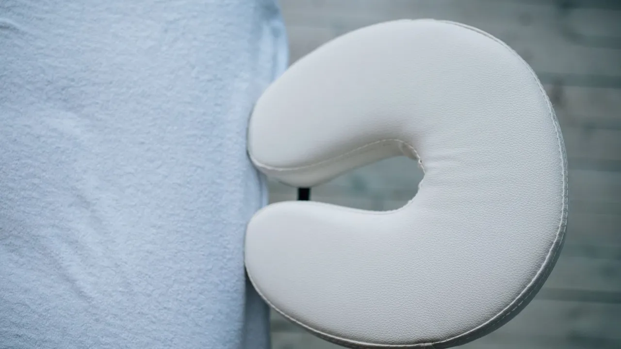 Une table de massage pliante noire installée dans un salon lumineux, avec serviettes et huiles.